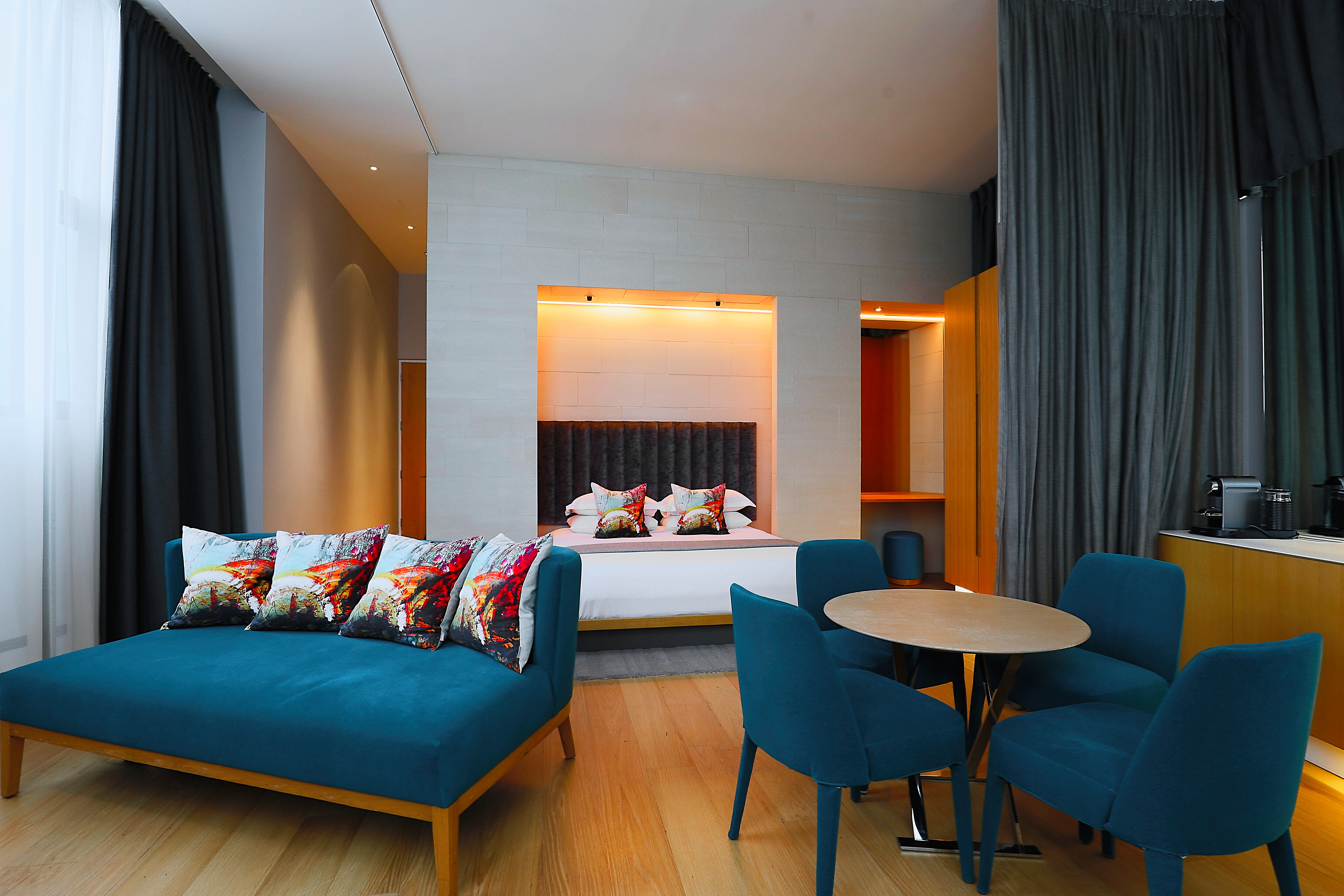 A well-furnished room featuring a comfortable bed, cozy couch, elegant table, and blue chairs.