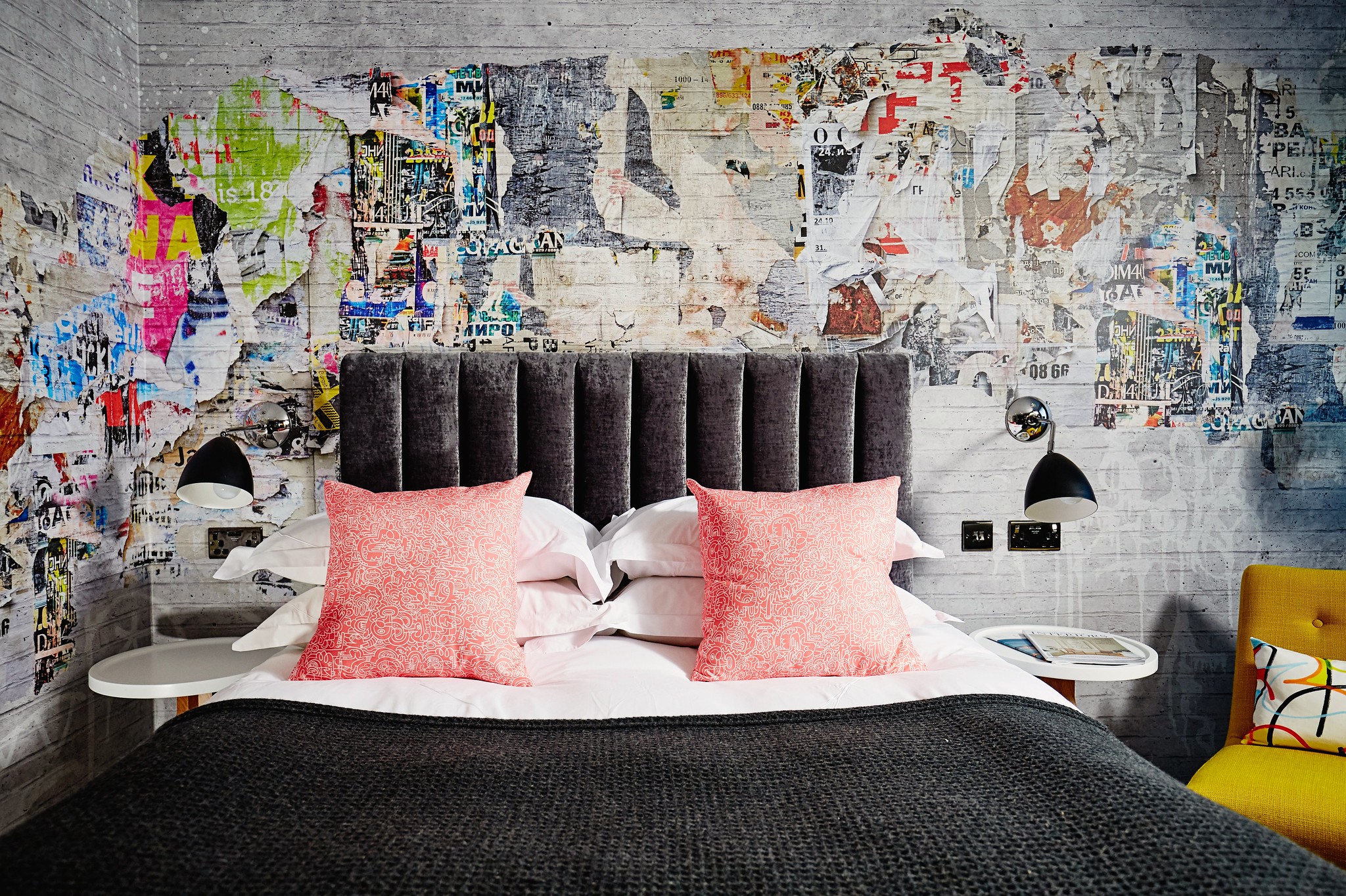 Grey bed with 2 pink pillows and a brightly decorated wall. 